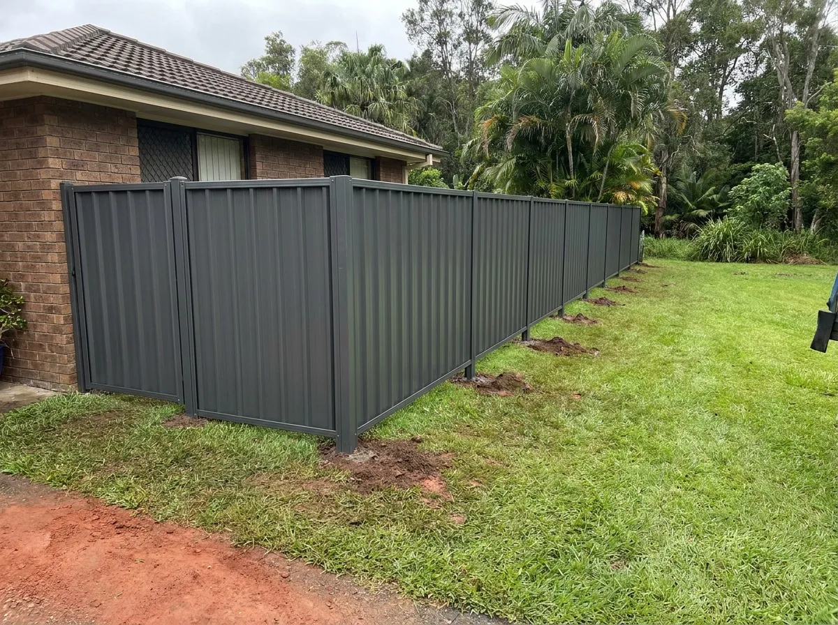 New dark grey Colorbond fence along the side of a brick home with lush green subtropical garden